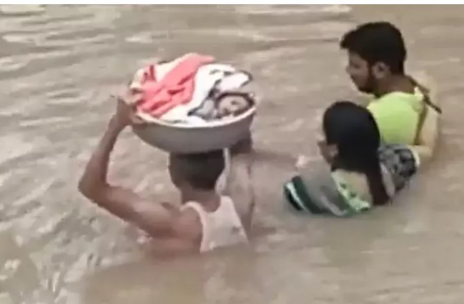 बाढ़ के पानी में फंस गया परिवार, देखें कैसे कृष्ण भगवान की तरह टोकरी में बच्चा रखकर ले जा रहा युवक