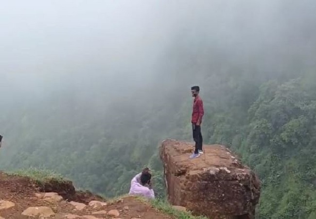 A young man risking his life and making photos and videos by standing on a mountain stone